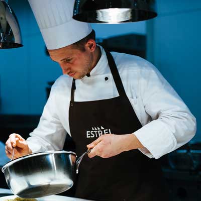 Estrel Hotel chef with black apron and chef's hat takes a dish from the pot